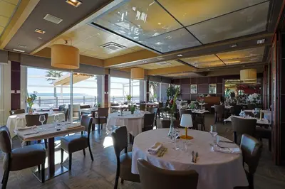 a restaurant with white tables and chairs and windows at Logis Hôtel & Restaurant Mediterranee in Port-la-Nouvelle