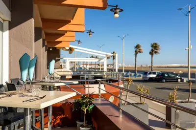 a restaurant with tables and chairs and the beach at Logis Hôtel & Restaurant Mediterranee in Port-la-Nouvelle