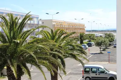 a white car parked in a parking lot with palm trees at Gites de France Bleu à la mer in Port-la-Nouvelle
