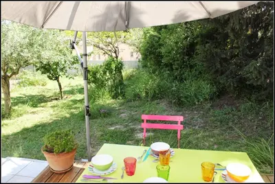 a table with an umbrella and a pink chair at Gîte du Fenouil in Lézignan-Corbières