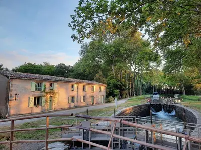 a canal in front of a building next to a building at La Bonne Planque - Maison éclusière de La Planque in Mas-Saintes-Puelles