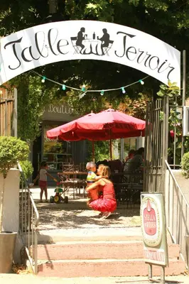 a woman sitting under a red umbrella in front of a restaurant at Contact Hôtel Le Minervois - Hôtel & Restaurant Au nord de Carcassonne in Caunes-Minervois