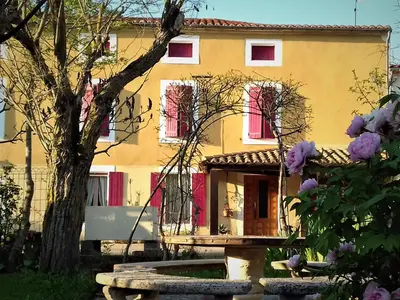 a yellow house with red windows and a tree at La Maison du Soleil in Saint-Gaudéric