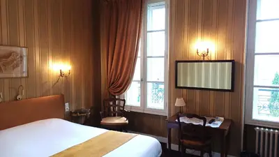 a bedroom with a bed and a desk and windows at Hotel Montsegur in Carcassonne