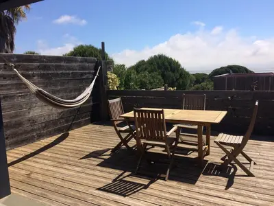 a wooden deck with a hammock and a wooden table and chairs at La Poussada, maisons écologiques avec vue mer in Lapalme