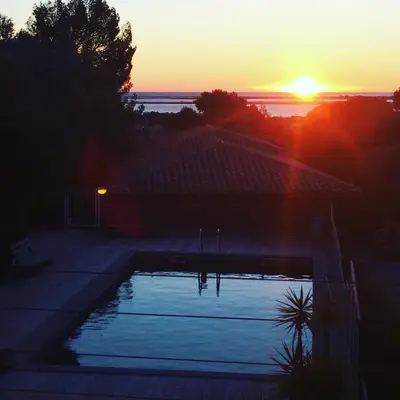 a sunset over a swimming pool in front of a house at La Poussada, maisons écologiques avec vue mer in Lapalme