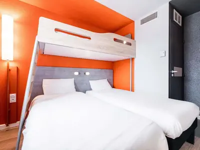 two beds in a bedroom with an orange wall at ibis budget Carcassonne Aéroport - A61 in Carcassonne