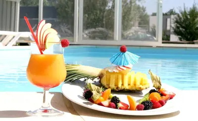 a plate of fruit and a drink next to a pool at Logis Hôtel - Auberge du Pastel - Hôtel 3 étoiles et Restaurant in Nailloux