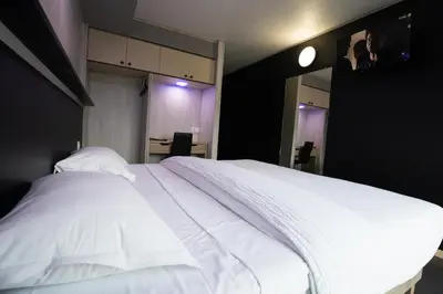 a bedroom with a white bed with a tv on the wall at Hôtel La Rocade in Pamiers