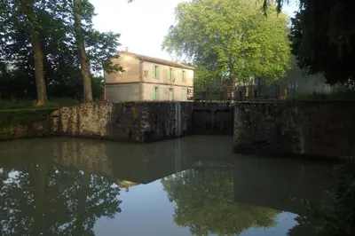 a building sitting next to a body of water at La Bonne Planque - Maison éclusière de la Domergue Canal du Midi in Mas-Saintes-Puelles