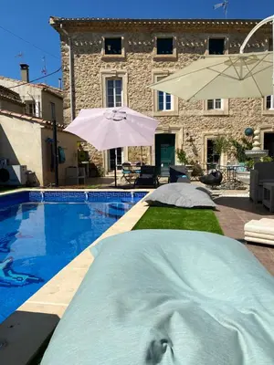 a swimming pool in front of a house with an umbrella at La Marelle chambre d hôtes à 500m du Canal du Midi in La Redorte