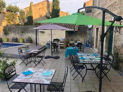 a patio with tables and chairs and an umbrella at La Marelle chambre d hôtes à 500m du Canal du Midi in La Redorte