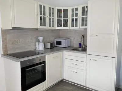 a white kitchen with white cabinets and a microwave at La petite maison bleue in Gruissan