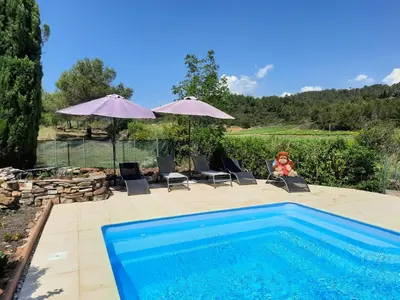 a pool with two umbrellas and a teddy bear sitting in a chair at Gite Charlrose at La Platriere in Cazedarnes