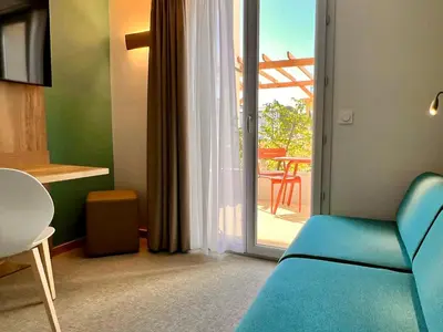 a room with a blue couch and a sliding glass door at The Originals City, Hôtel Le Puech, Narbonne in Narbonne