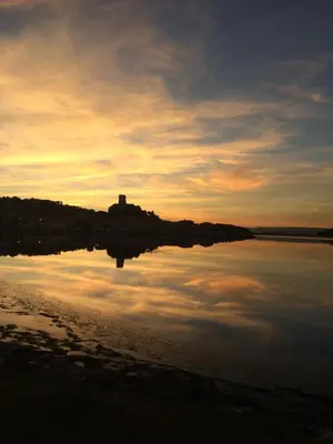a sunset over a body of water with a castle in the distance at La Belle Gruissanaise in Gruissan