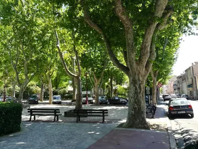 a park with benches and trees on a city street at Appartement avec Terrasse in Narbonne