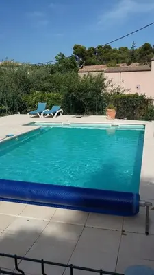 a blue swimming pool with two chairs and a house at Maison du Charron in Azillanet