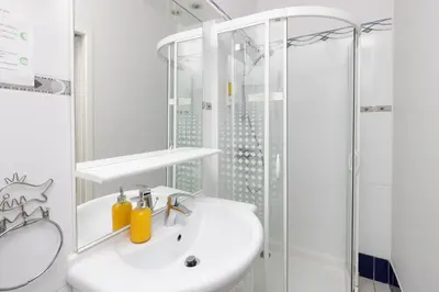 a white bathroom with a shower and a sink at Le Grand Bassin in Castelnaudary