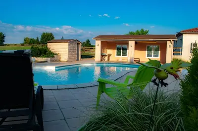 a swimming pool with a green chair and a house at Gîte Lempery in Puéchoursi