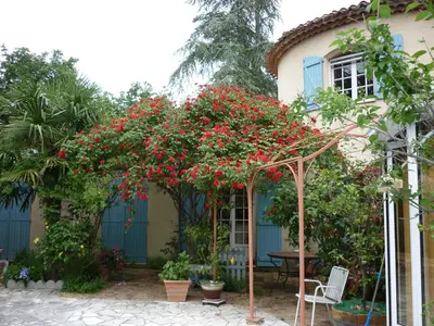 a pergola with red flowers in front of a house at LES BRUYERES chambre d'hôte de charme Calme assuré in Loupia
