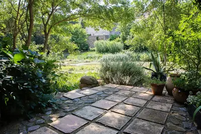 a garden with a stone patio with plants and trees at The Balcony Gîte - Riverside Lagrasse in Lagrasse
