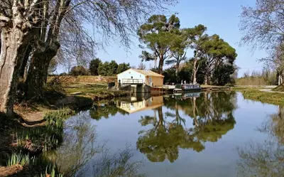 a lake with a house and a boat in it at Gîte proche du canal du midi et Narbonne 2 chambres in Mirepeisset