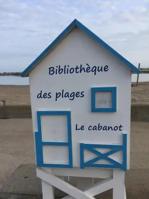 a blue and white sign sitting on the beach at T 3 appart les jardins du phœbus in Gruissan
