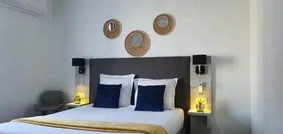 a bedroom with a large bed with blue pillows and mirrors at Hôtel L'Alsace in Narbonne
