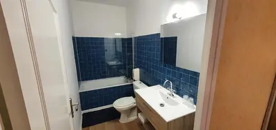 a blue tiled bathroom with a toilet and a sink at Hôtel L'Alsace in Narbonne