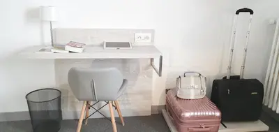 a desk with a laptop and a suitcase and a chair at Hôtel L'Alsace in Narbonne