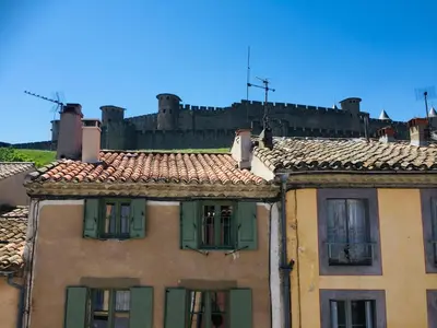 a building with green shutters and a castle in the background at Au pied de la Cité in Carcassonne