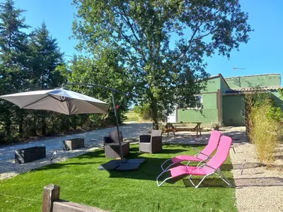 a couple of pink chairs and an umbrella in the grass at gite tout confort in Montolieu