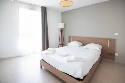 a white bedroom with a large bed with white sheets at Zenitude Hôtel-Résidences Narbonne Centre in Narbonne