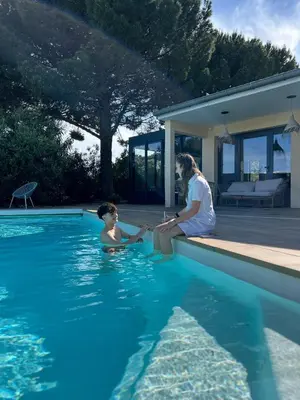a man sitting next to a child in a swimming pool at Kyriad Carcassonne - Aéroport in Carcassonne