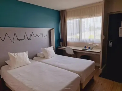 a bedroom with two beds and a desk with a window at Kyriad Carcassonne - Aéroport in Carcassonne