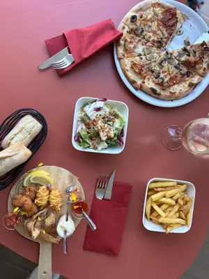 a table with plates of food and a pizza and french fries at Kyriad Carcassonne - Aéroport in Carcassonne