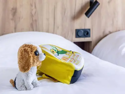 a stuffed dog sitting on a bed with a bag at Greet Hôtel Castres Saix in Saix