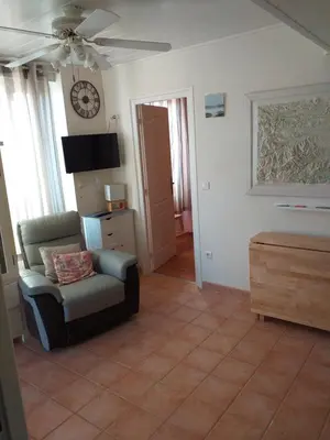 a living room with a chair and a clock on the wall at ALBASUD - Appartement meublé avec terrasse - Salses le Chateau 66 in Salses-le-Chateau
