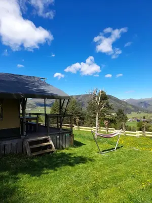 a hammock and a house with mountains in the background at Chalet et mobil homes dans la montagne au Camping les Sapins in Camurac