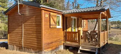 a wooden cabin with chairs on the porch at Chalet et mobil homes dans la montagne au Camping les Sapins in Camurac