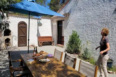 a woman standing next to a table with a blue umbrella at Villa w Garden & Guest House in Prades-sur-Vernazobre