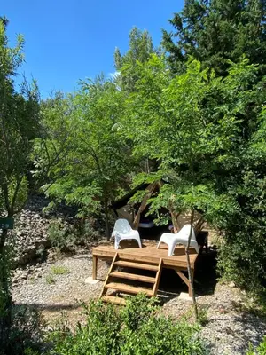 a tent with two white chairs in the woods at Camping la Peiriere - Lodge en Pays Cathare in Tuchan