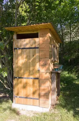 a wooden outhouse with a door in the grass at Ma caravane dans les collines in Villeneuve-la-Comptal