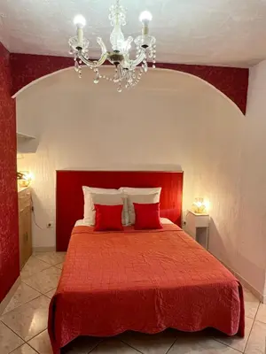 a bedroom with a red bed with a chandelier at Bed & Breakfast Le Beauséjour in Carcassonne