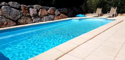 a swimming pool with two chairs and a rock wall at La villa marquesa in Fitou