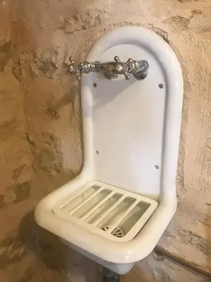 a white urinal in a stone wall with a drain at Gites de Montcabirol in Mirepoix