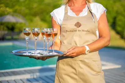 a woman holding a tray with three wine glasses at Domaine de Merlac in Rieussec