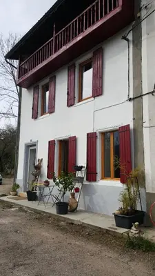 a white house with red shuttered windows and potted plants at El roble in LʼAiguillon