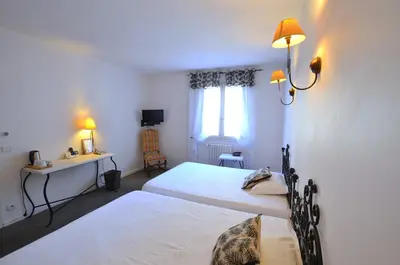 a bedroom with two beds and a desk and a window at Logis Hôtels - Hôtel Restaurant du Midi in Revel